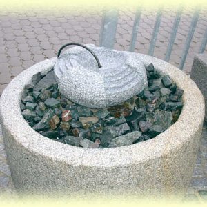 Kaskadenförmig bearbeiteter  Granit-Quellstein auf Basaltschotter in       rundem Natursteinbecken aus Granit (Durchm. 90, Höhe 40 cm).